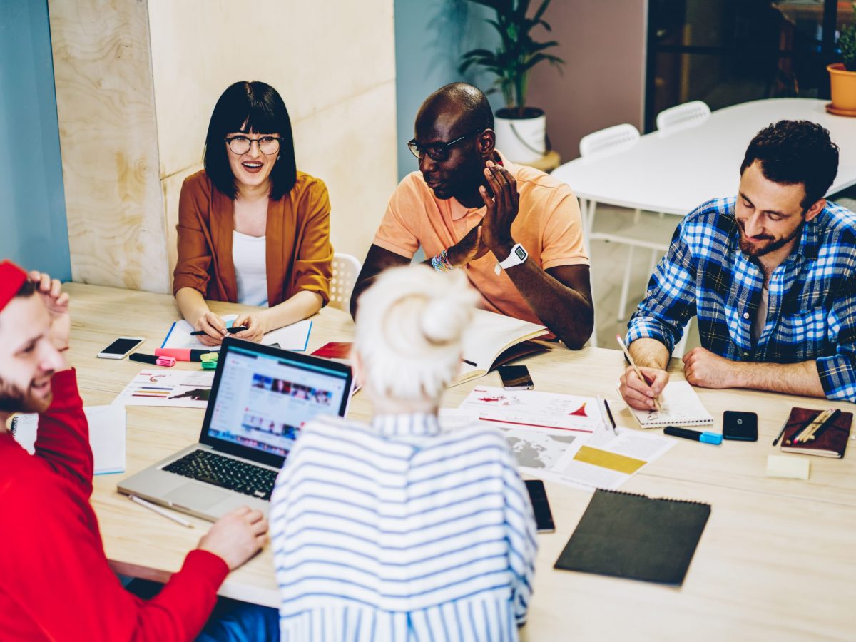 Multicultural group of young people dressed in smart casual wear communicating with each other and discussing project having brainstorming meeting in office.Collaboration process of modern employees
