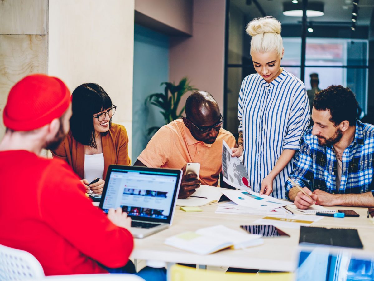 Multicultural group of creative young people collaborating on discussing graphic sketches during brainstorming.Diverse male and female employees in smart casual wear cooperating in modern office