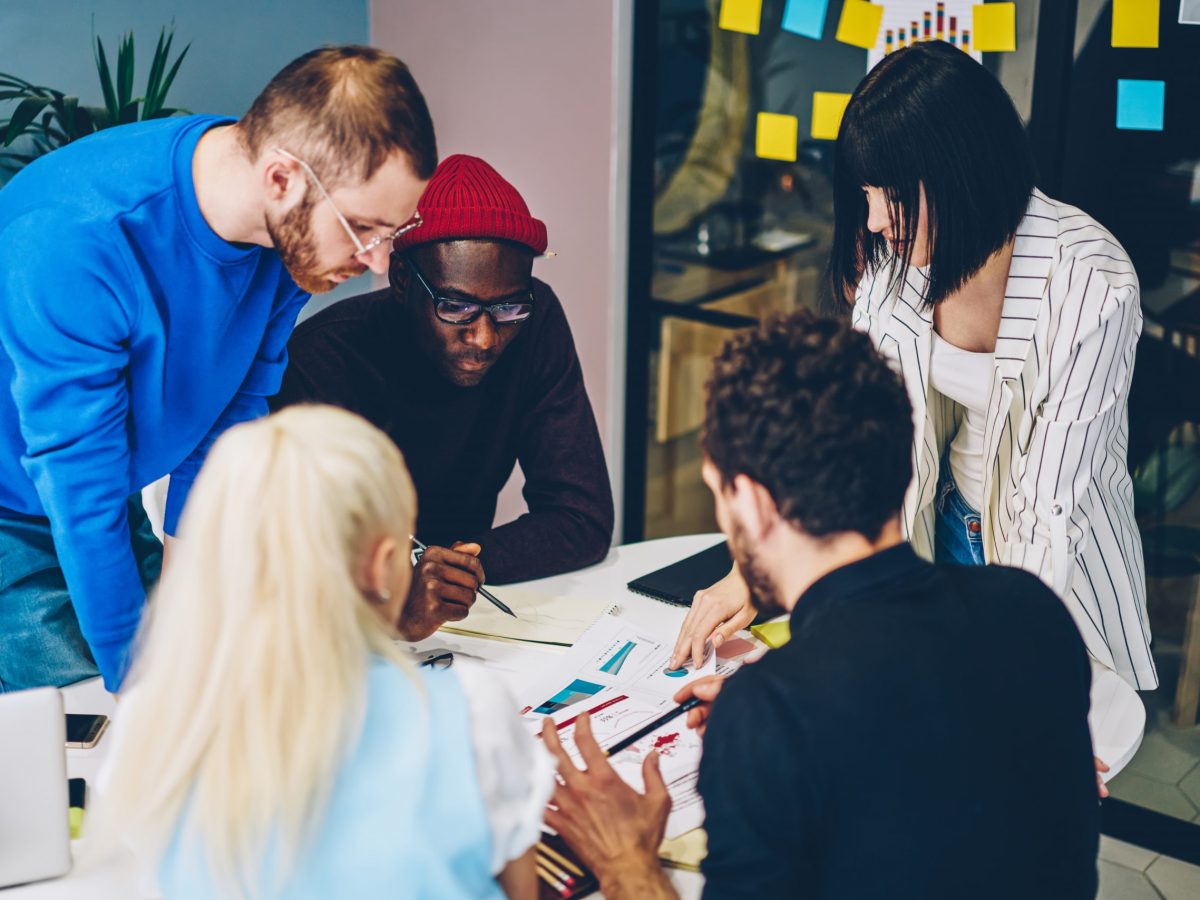 Diverse group of young people dressed in smart casual wear discussing productive strategy of collaborative process sitting at meeting table during brainstorming.Hipster students teamworking on task