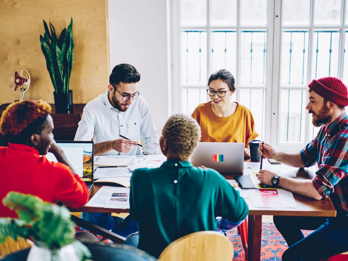 Skilled young male and female employees brainstorming during meeting table using technology and wifi in office,multiracial crew of colleagues smiling satisfied with productive cooperation on job
