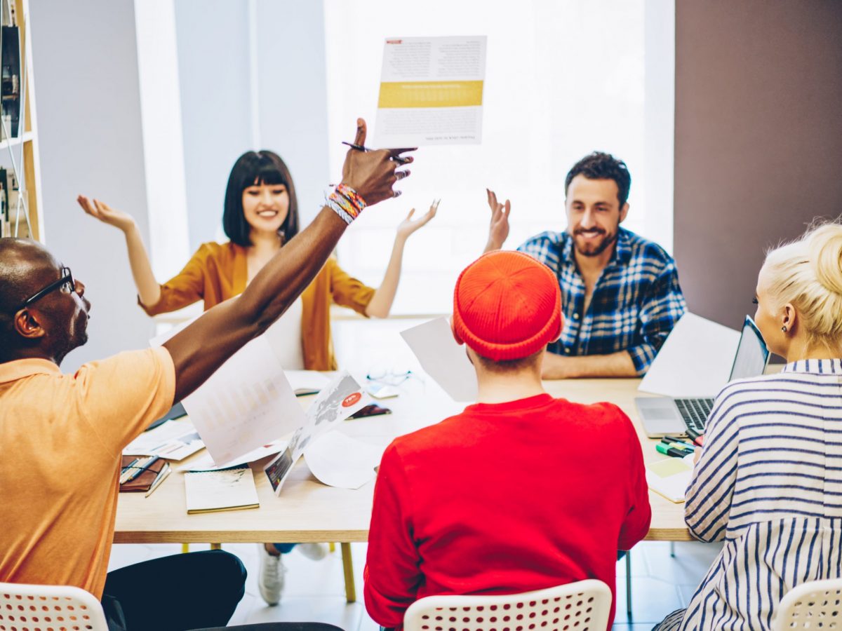 Happy multiracial crew of employees celebrating completing successful project in cooperation, overjoyed team of male and female coworkers excited with result of brainstorming session at meeting